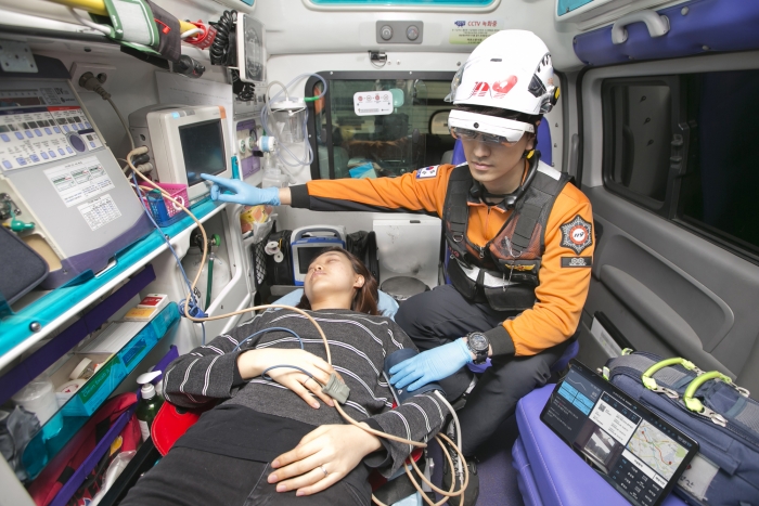 119 구급차 안에서 구급대원이 5G AR 글래스와 360도 카메라로 병원 의료진과 대화하며 환자를 돌보고 있다.