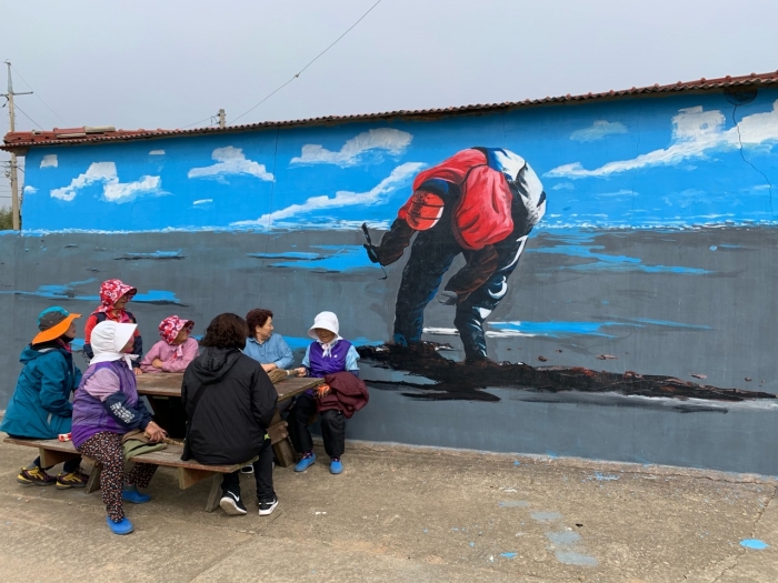 박종만 화가의 갯벌을 주제로한 탄도의 담벼락 벽화를 마을 주민들이 바라보고 있다.