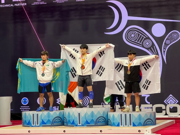 (사진=19일 열린 아시아주니어역도선수권에서 우승한 신록(가운데)이 시상대에서 태극기를 펼쳐 보이고 있다. 오른쪽은 용상 3위 조민재 / 대한역도연맹)